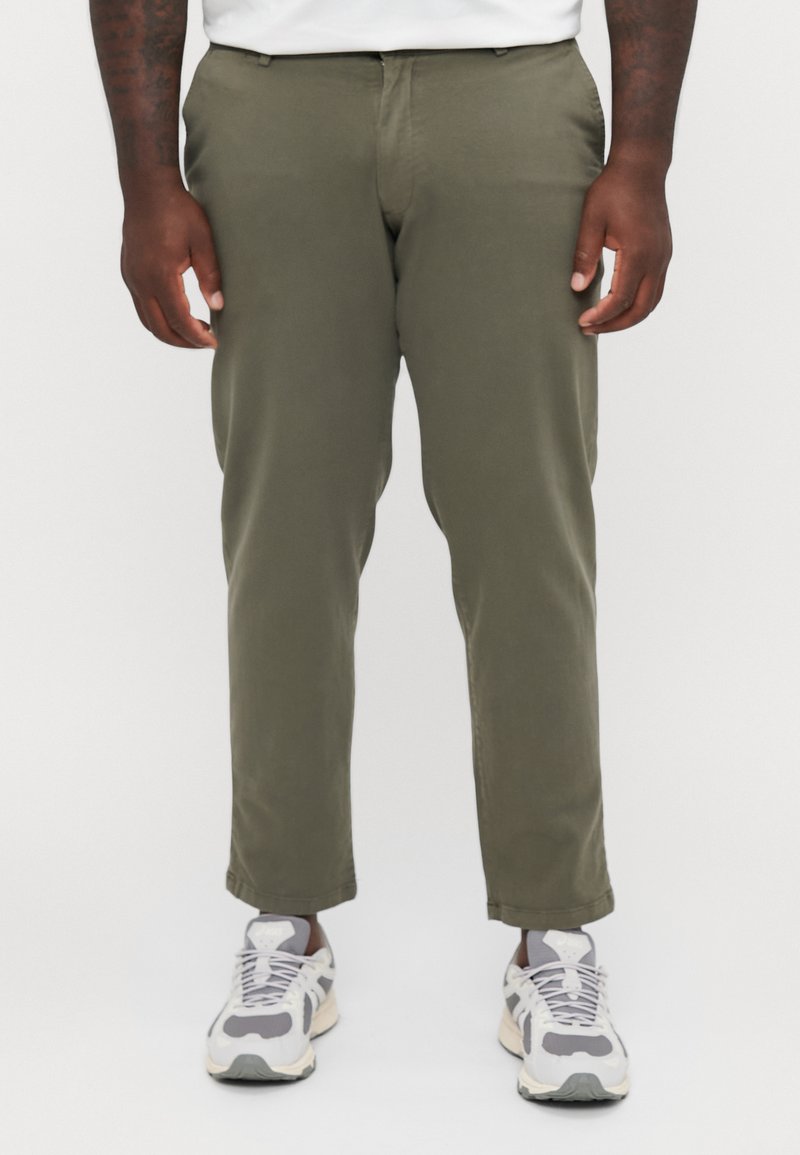 Pantalones tailored en verde oliva, con una textura suave y corte recto, combinados con zapatillas gris y blanco.