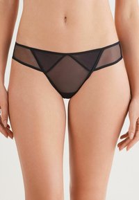 Zwarte semi-transparante hipsteronderbroek met geometrische uitsparingen, zachte mesh-stof en een gladde tailleband voor een modern ontwerp.
