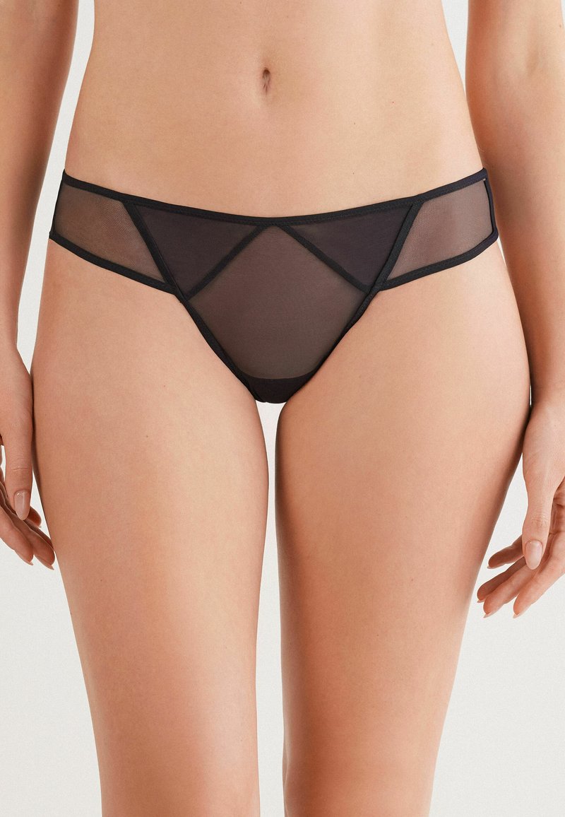 Zwarte semi-transparante hipsteronderbroek met geometrische uitsparingen, zachte mesh-stof en een gladde tailleband voor een modern ontwerp.