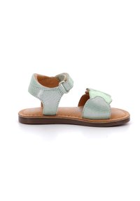 Sanda blanca menta con un acabado metálico, correa ajustable y un acento decorativo en forma de hoja. Suela marrón plana y interior acolchado.
