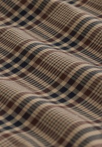 Close-up of soft fabric with beige, brown, and black plaid pattern featuring small and large checkered designs on wavy surface.
