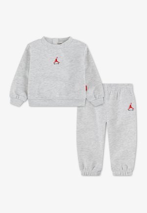 Jasnoszary dres dziecięcy z bluzą z długim rękawem i spodniami dresowymi, oba z małym czerwonym logo Air Jordan na piersi i biodrze.