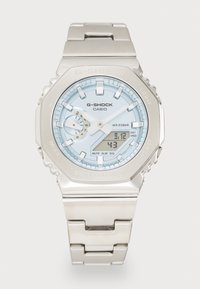Casio G-Shock watch with a silver stainless steel band, light blue dial, digital display, and silver accents. Water-resistant to 20 bar.