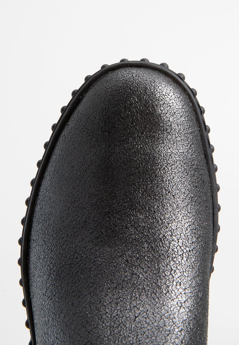Schwarzes Schuhwerk mit einer strukturierten, glänzenden Oberfläche. Verfügt über eine abgerundete Zehe und eine erhöhte, gepunktete Verzierung entlang der Sohle.