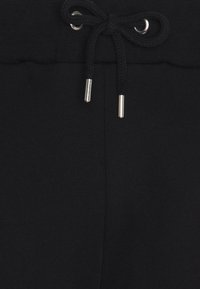 Schwarze Jogginghose mit Kordelzugbund und silbernen Metallenden, weicher Textur und taillierter Passform.