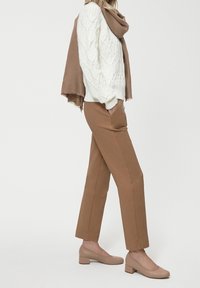 Pull en tricot blanc avec motif en câble, écharpe marron, pantalon kaki et chaussures à talons block beiges. Vue de côté, présenté sur un fond clair.