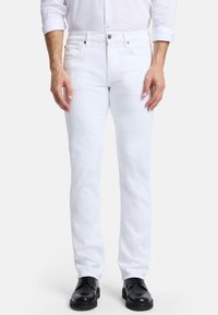 Jean en denim blanc à coupe slim, avec un design classique à cinq poches et des détails de couture subtils, associés à des chaussures noires.