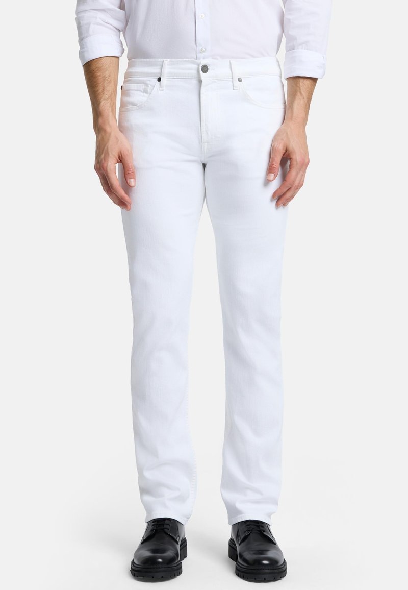 Jean en denim blanc à coupe slim, avec un design classique à cinq poches et des détails de couture subtils, associés à des chaussures noires.