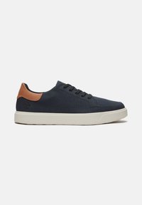 Marineblauwe canvas sneaker met bruine leren accenten, witte rubberen zool, ronde neus, vetersluiting en logodetail aan de zijkant.