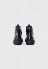 Botas de tobillo de cuero negro con un acabado suave, puntera redondeada y una suela gruesa con dibujo. Presentan un cierre lateral con cremallera y tiradores en la parte trasera.