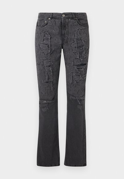 Μαύρο τζιν με άνοιγμα στο κάτω μέρος, με πολλές φθορές και σκισίματα στα μπροστινά μηριαία μέρη και τα γόνατα.