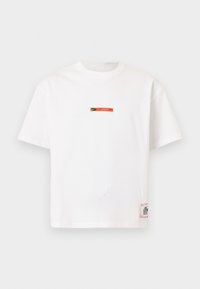 Λευκό T-shirt Nike με κοντά μανίκια και μικρό λογότυπο "Fussball" σε μαύρο και κόκκινο στο στήθος, καθώς και ορθογώνια ετικέτα κοντά στο κάτω τελείωμα.