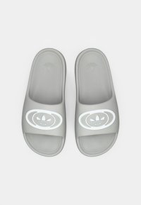 Halli libisevad sandaalid tekstuurse pinnaga, millel on valge logo ja rihmal ümmargused aktsendid. Lame disain ja avatud varba stiil.