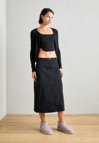 Top negro corto con textura acanalada, falda negra hasta la rodilla con bolsillo frontal y botas de tobillo de color púrpura claro con tela suave.