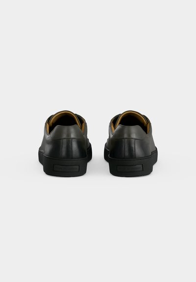 Ζευγάρι μαύρα δερμάτινα sneakers χαμηλού τύπου με καφέ εσωτερική επένδυση, εμφανιζόμενα από πίσω σε απλό λευκό φόντο.