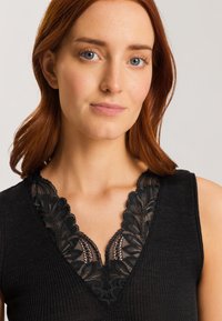 Schwarzes, geripptes Tanktop mit einem gewellten Spitzenausschnitt. Die Textur ist glatt und das Design ist enganliegend, sodass es sich perfekt an den Körper anschmiegt.