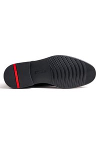 Semelle en caoutchouc noir avec des rainures horizontales et verticales ; présente une bande d'accent rouge et un nom de marque en relief. Design durable et texturé.