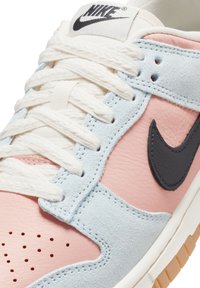 Närbild av rosa och ljusblå Nike-sneakers med vita snören, svart swoosh-logotyp och perforeringar på tåområdet.