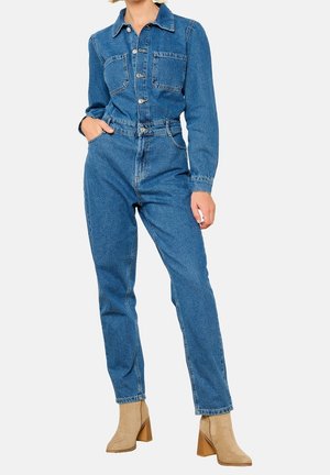 Kombinezon dżinsowy w średnim niebieskim kolorze z długimi rękawami, zapinany na guziki z przodu, z dwoma kieszeniami na piersi i dopasowaną talią. Połączony z beżowymi botkami za kostkę.