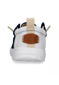 Scarpa bianca e blu navy con un pull tab beige, dettaglio in pelle con etichetta "HEY DUDE" e suola bianca texturizzata.