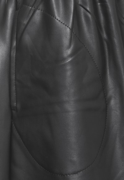 Il tessuto in pelle nera presenta una spiccata tasca circolare, una texture liscia e una leggera lucentezza. Il design include dettagli di cucitura lungo i bordi.
