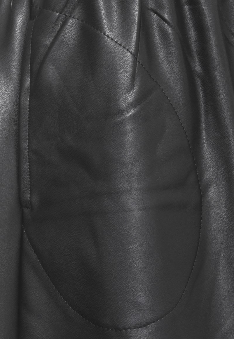 Il tessuto in pelle nera presenta una spiccata tasca circolare, una texture liscia e una leggera lucentezza. Il design include dettagli di cucitura lungo i bordi.