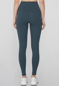 Leggings de tiro alto en color azul marino, hechos de un material elástico, con una textura suave y un diseño ajustado, combinados con zapatillas deportivas blancas.