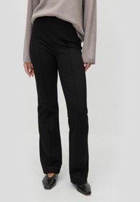 Svarta utsvängda byxor med en slät tyg, flat framsida och sidofickor, som bärs med en ljusgrå oversized topp och svarta skor.