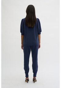 Námořnický modrý koordinovaný outfit složený z volného topu s nabíranými rukávy a odpovídajícími tapered kalhotami, vyrobený z měkké tkaniny, nošený s podpatečními sandály.