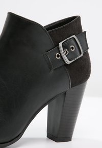 Stivale alla caviglia nero con tacco alto, realizzato con una combinazione di pelle liscia e camoscio, con un accento di fibbia argentata sul lato.