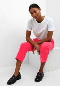 Witte short-sleeve t-shirt, felroze cropped broek en zwarte loafers. Eenvoudig ontwerp met gladde stof en strakke lijnen.