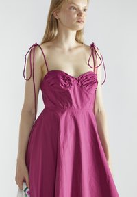 Fuchsia jurk met een getailleerd lijfje met gerimpelde accenten en verstelbare bandjes op de schouders, uitlopende rok met een gladde textuur.