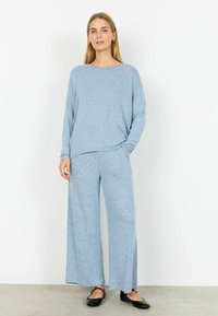 Jasnoniebieska, miękka dzianinowa bluzka z długim rękawem o luźnym kroju i okrągłym dekolcie, zestawiona z pasującymi szerokimi spodniami. Płaskie czarne buty.