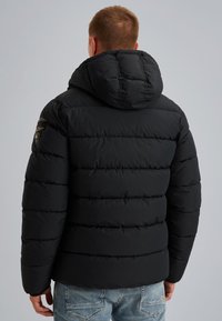 Giacca a vento nera con cuciture orizzontali, cappuccio e una toppa sulla spalla sinistra. Texture morbida e trapuntata con un design aerodinamico.
