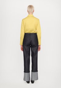 Gul langermet skjorte kombinert med mørk denim vide bukser med en kontrasterende grå hem. Glatt stoff med skreddersydd passform.