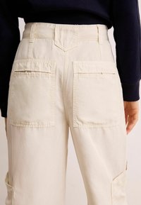 Pantaloni cargo bej cu talie înaltă, două buzunare mari la spate și o textură netedă. Cusăturile vizibile accentuează designul, iar croiala relaxată oferă confort.