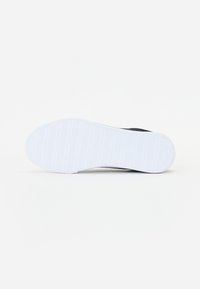 Mustade sneakerite välistald, mis näitab tekstuurset valget kummist pinnakatet horisontaalsete soontega, mis on loodud haardumise ja pidamise tagamiseks. Puhta disainiga, millel on minimaalne detailide hulk.