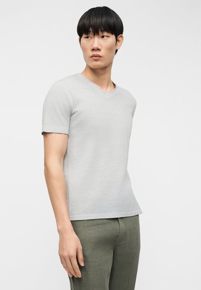 Ανοιχτό γκρι κοντομάνικη μπλούζα V-λαιμόκοψη από μαλακό ύφασμα. Διαθέτει κλασική εφαρμογή και απαλή υφή, συνδυασμένη με πράσινο παντελόνι.