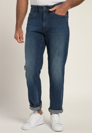 Mørkeblå denimjeans med lige pasform, opsmøget ved anklerne, med fem lommer og lynlås foran, båret med hvide sneakers.