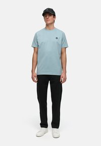 Ljusblå bomulls-t-shirt med rund halsringning och en liten broderad logotyp, tillsammans med svarta byxor och vita sneakers. Kaps har en mönstrad design.