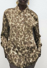 Brown leopard-print button-up shirt with a pointed collar, long sleeves, and smooth, silky texture. Includes front pocket detail.
