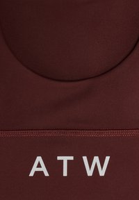 Gros plan sur un tissu bordeaux avec une couture cousue et les lettres blanches "ATW" imprimées sous la couture.