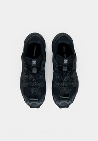 Čierne športové topánky s textúrovaným povrchom, zaoblenou špičkou a protišmykovou podrážkou. Na vrchu sú viditeľné  šnúrky a detaily loga.