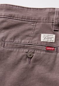 Pantalon Levi's en tissu violet doux à la texture lisse. Comprend une poche arrière avec un bouton et une étiquette de marque cousue sur la ceinture.