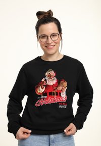 Felpa nera con una grafica vintage di Babbo Natale che tiene una bottiglia. Il testo dice "...e un Buon Natale a tutti, Coca-Cola."