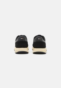 Scarpe sportive nere con una tomaia in suede e materiale sintetico, suola in gomma e suola di trazione beige. Presentano un branding minimal sul retro.