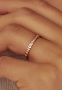 Bague en or rose fin ornée d'une rangée de petites pierres étincelantes le long de la bande, sur fond de peau claire.