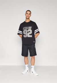 Camiseta de algodón negra con impresión plateada "Champion 92", mangas cortas a rayas. Combinada con pantalones cortos negros y zapatillas blancas.
