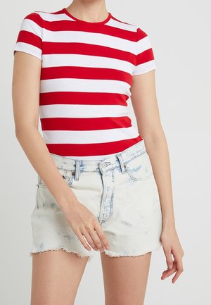 Femme portant un t-shirt à manches courtes rayé horizontalement rouge et blanc et un short en jean bleu clair avec des ourlets effilochés.