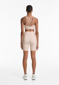 Lichtbeige sportset met een sportbeha met spaghettibandjes en een kruislings rugpand, en hoge taille short, beide gemaakt van soepele, elastische stof.
